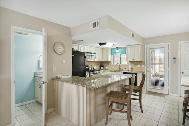 kitchen with a kitchen breakfast bar, sink, appliances with stainless steel finishes, light stone counters, and kitchen peninsula