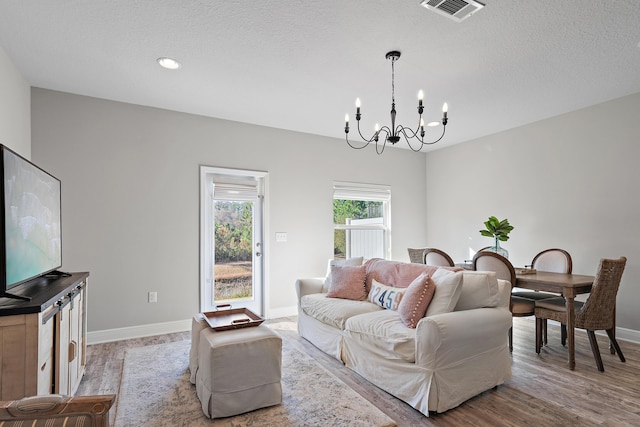 living room with an inviting chandelier, a textured ceiling, and light wood-type flooring