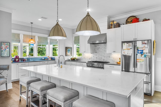 kitchen with sink, backsplash, stainless steel appliances, a center island with sink, and wall chimney exhaust hood