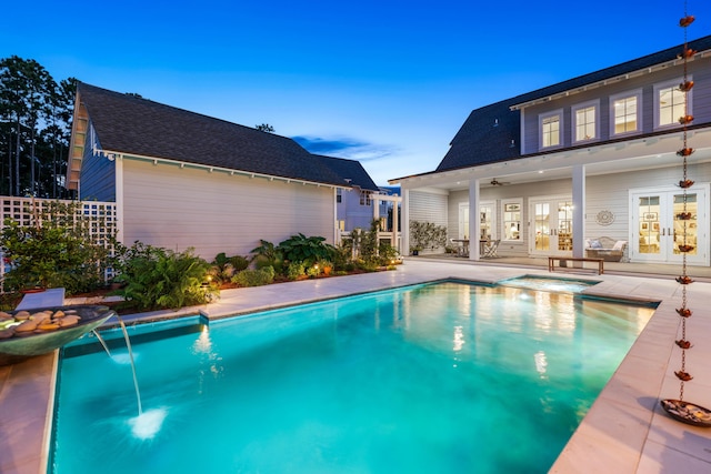 pool at dusk with a patio, pool water feature, ceiling fan, and french doors