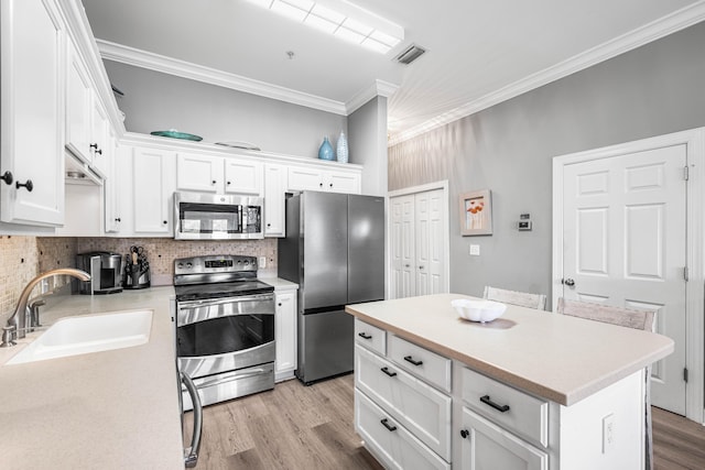 kitchen with ornamental molding, stainless steel appliances, sink, a center island, and white cabinetry