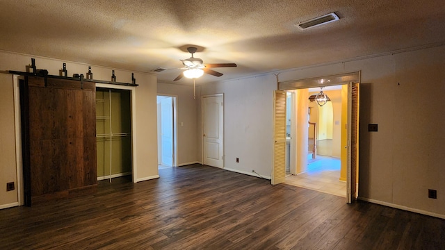 unfurnished bedroom with ceiling fan, a barn door, a textured ceiling, dark hardwood / wood-style flooring, and multiple closets