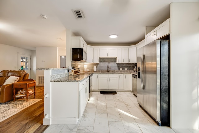 kitchen featuring marble finish floor, appliances with stainless steel finishes, white cabinets, a sink, and a peninsula