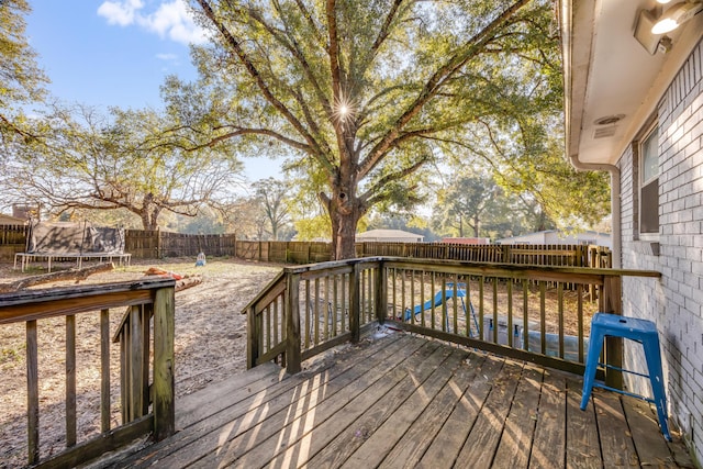 wooden deck with a fenced backyard and a trampoline