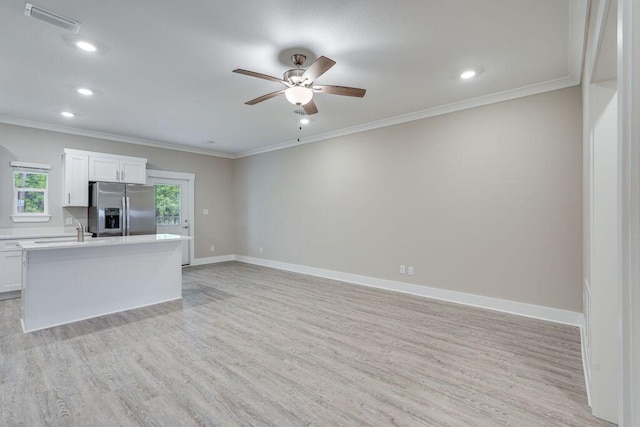 kitchen featuring stainless steel fridge, a center island with sink, white cabinetry, and a wealth of natural light