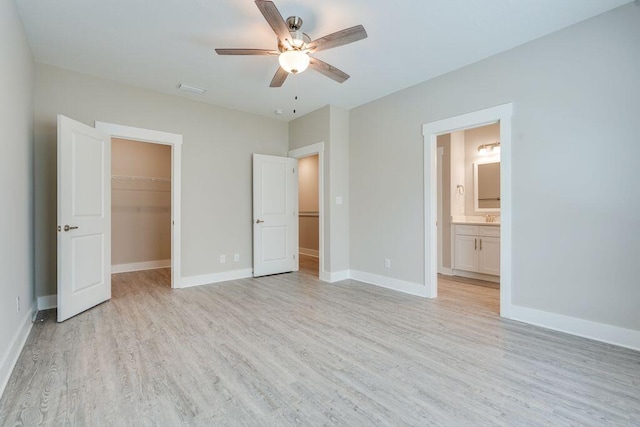 unfurnished bedroom with ensuite bath, ceiling fan, a walk in closet, a closet, and light wood-type flooring