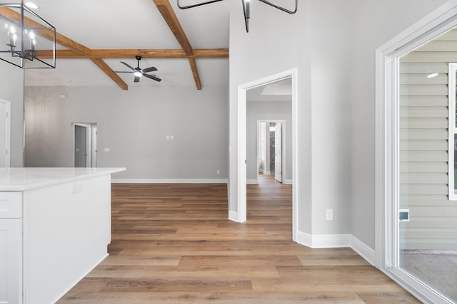 unfurnished living room with beam ceiling, ceiling fan with notable chandelier, light hardwood / wood-style floors, and coffered ceiling