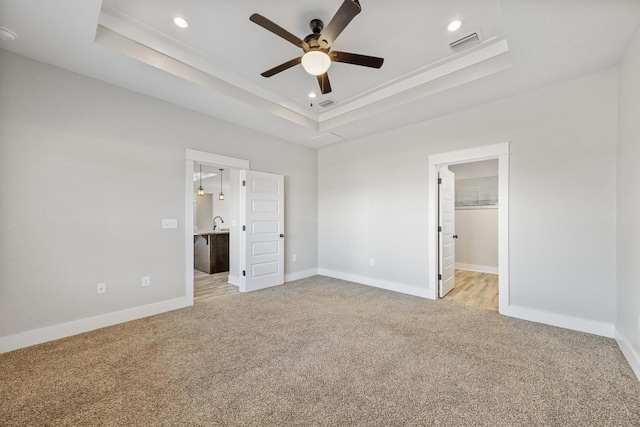 unfurnished bedroom with light carpet, ceiling fan, a spacious closet, a tray ceiling, and a closet