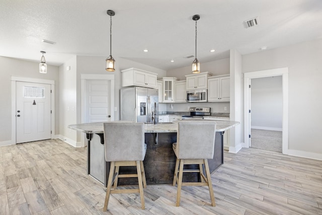 kitchen featuring a large island with sink, white cabinetry, hanging light fixtures, and appliances with stainless steel finishes