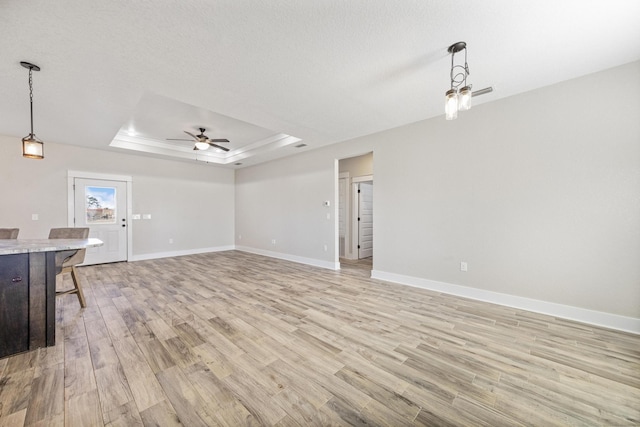 unfurnished living room featuring a raised ceiling, ceiling fan, light hardwood / wood-style floors, and a textured ceiling