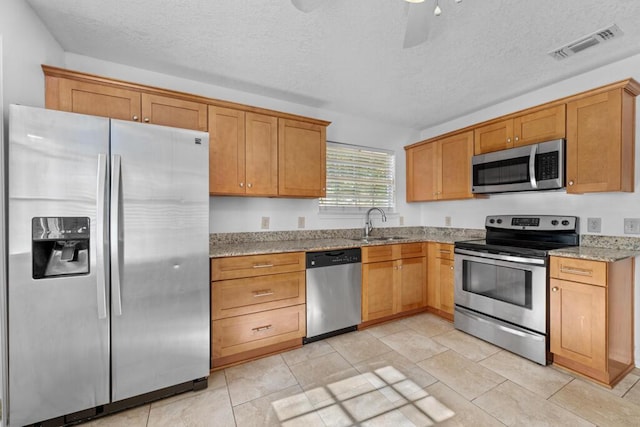 kitchen featuring light stone countertops, sink, ceiling fan, a textured ceiling, and appliances with stainless steel finishes