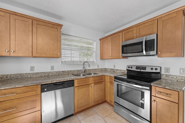 kitchen featuring sink, light stone countertops, a textured ceiling, light tile patterned flooring, and stainless steel appliances