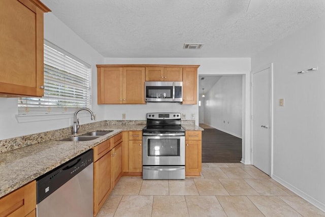 kitchen with light stone countertops, a textured ceiling, stainless steel appliances, sink, and light tile patterned floors