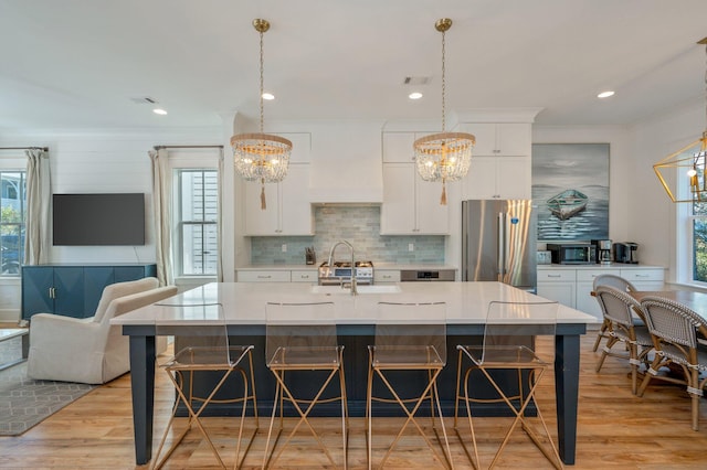 kitchen with white cabinetry, stainless steel fridge, hanging light fixtures, and a spacious island