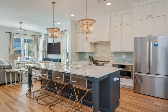 kitchen featuring decorative backsplash, appliances with stainless steel finishes, a breakfast bar, a kitchen island with sink, and white cabinetry