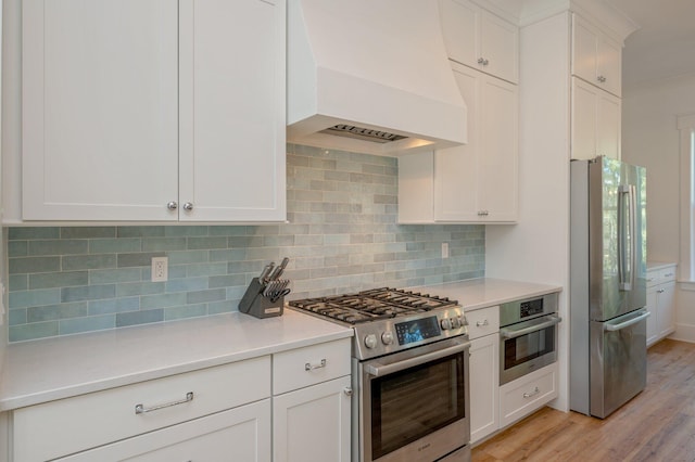 kitchen with appliances with stainless steel finishes, premium range hood, white cabinetry, and tasteful backsplash