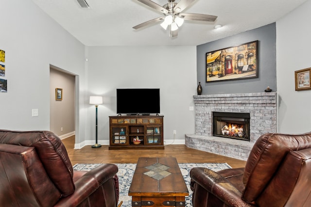 living room with a brick fireplace, wood-type flooring, and ceiling fan