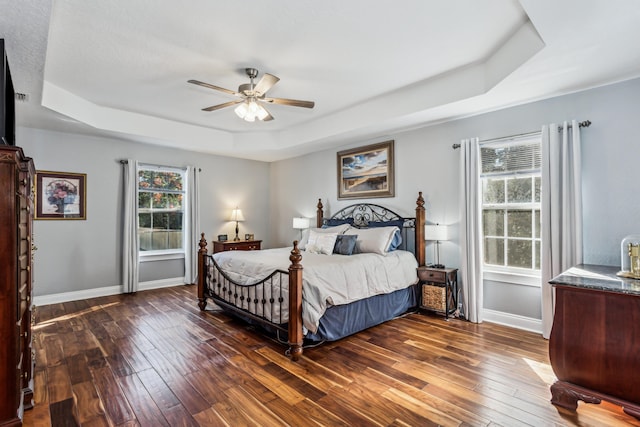 bedroom with a tray ceiling, dark wood-type flooring, and ceiling fan