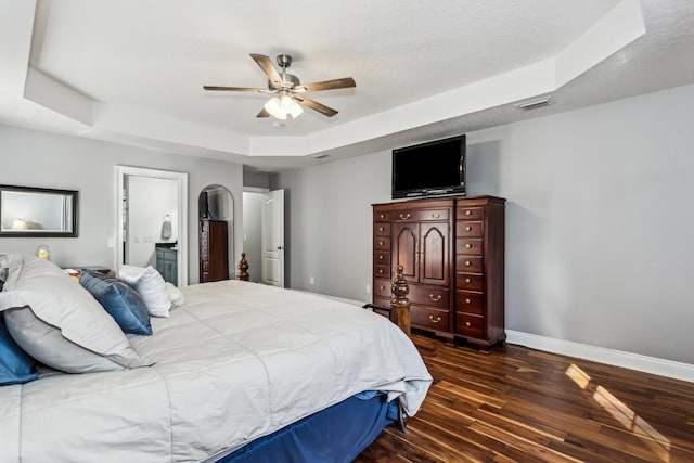 bedroom with ceiling fan, connected bathroom, dark hardwood / wood-style flooring, and a raised ceiling