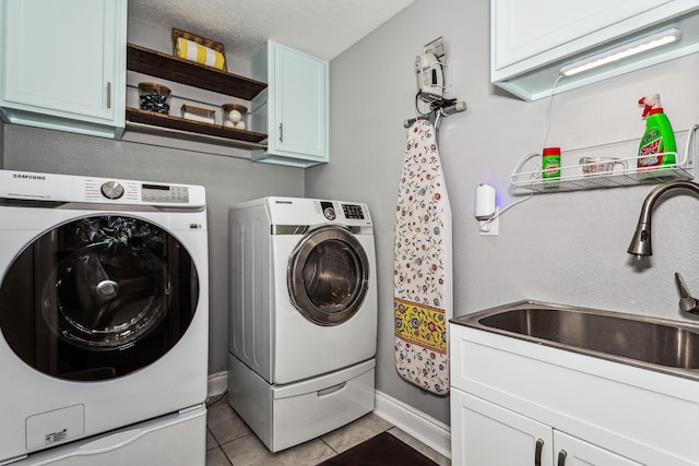 laundry area with sink, light tile patterned floors, washer and clothes dryer, cabinets, and a textured ceiling