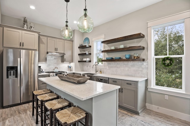 kitchen featuring gray cabinetry, light stone countertops, light hardwood / wood-style flooring, a kitchen island, and appliances with stainless steel finishes