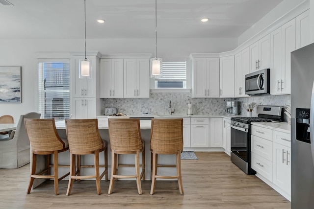 kitchen with tasteful backsplash, decorative light fixtures, a breakfast bar area, white cabinets, and appliances with stainless steel finishes