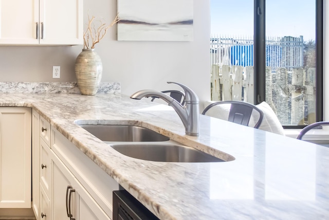 kitchen with light stone countertops, white cabinets, and sink