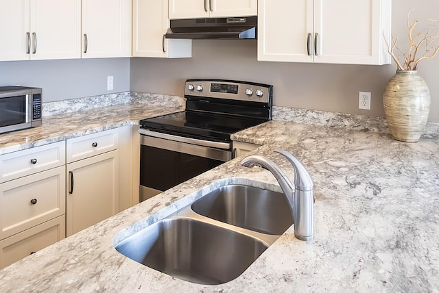 kitchen with light stone counters, stainless steel appliances, white cabinets, and sink