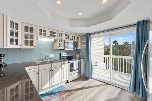 kitchen with white cabinets, a raised ceiling, sink, light wood-type flooring, and stainless steel appliances