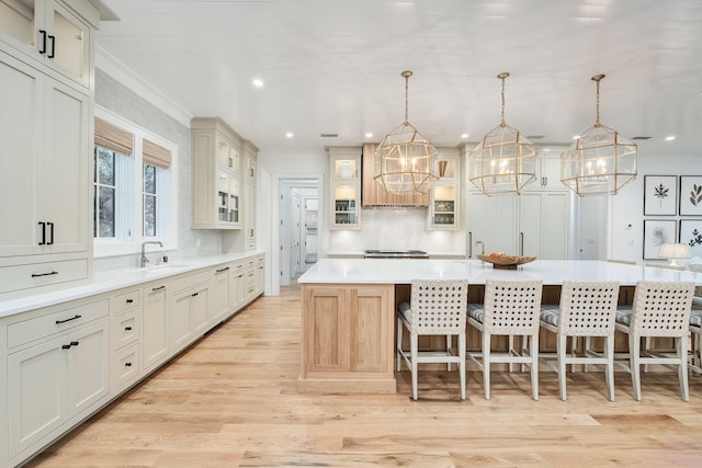kitchen with glass insert cabinets, a sink, crown molding, light countertops, and decorative backsplash