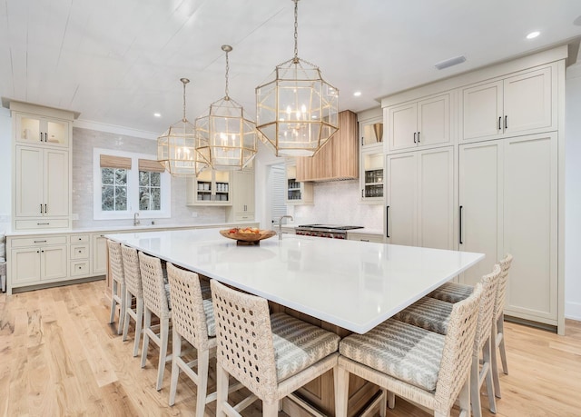 kitchen with an inviting chandelier, light wood finished floors, glass insert cabinets, and visible vents