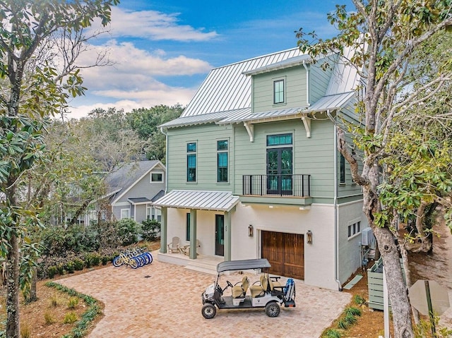 back of house featuring an attached garage, metal roof, decorative driveway, a balcony, and a standing seam roof