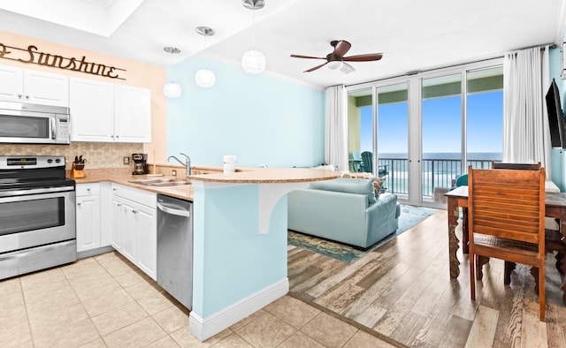 kitchen with kitchen peninsula, decorative backsplash, stainless steel appliances, sink, and hanging light fixtures