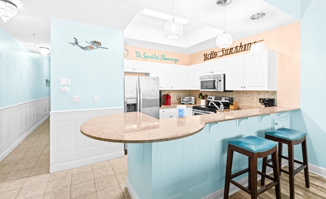 kitchen featuring kitchen peninsula, white cabinets, decorative light fixtures, and appliances with stainless steel finishes