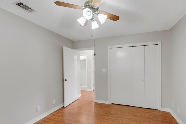 unfurnished bedroom with a textured ceiling, light wood-type flooring, a closet, and ceiling fan