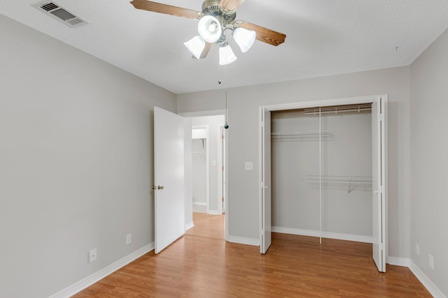 unfurnished bedroom featuring ceiling fan, a closet, a textured ceiling, and light wood-type flooring