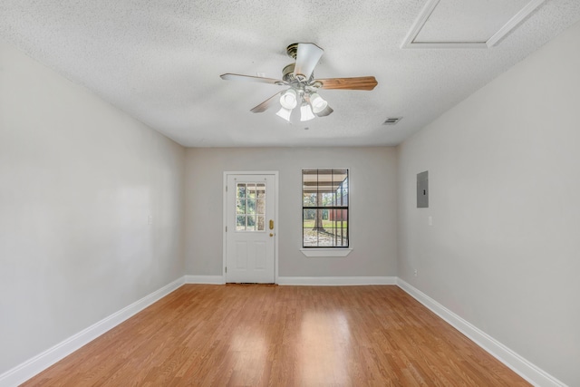 empty room featuring ceiling fan, light wood-type flooring, a textured ceiling, and electric panel