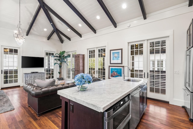 kitchen with french doors, stainless steel dishwasher, a kitchen island with sink, sink, and lofted ceiling with beams