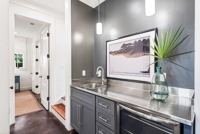 bar with sink, hanging light fixtures, gray cabinets, stainless steel counters, and beverage cooler