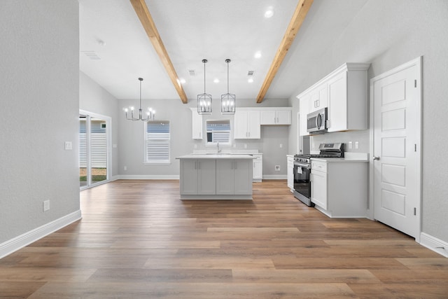 kitchen with stainless steel appliances, beam ceiling, decorative light fixtures, white cabinets, and an island with sink