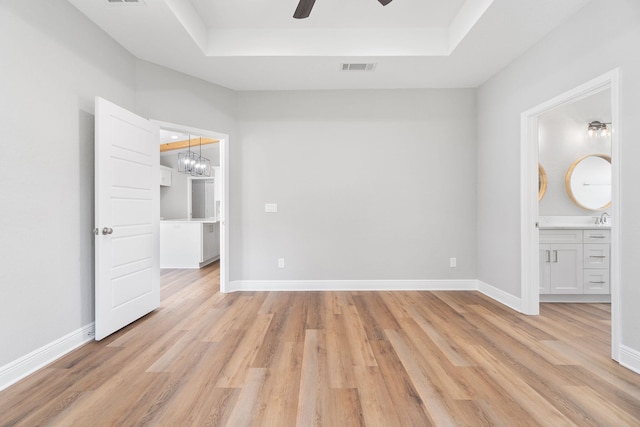 unfurnished bedroom with a tray ceiling, ceiling fan, sink, connected bathroom, and light hardwood / wood-style floors