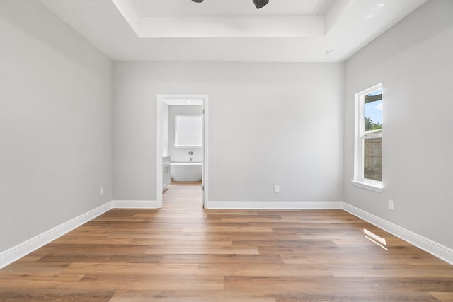 unfurnished bedroom featuring ceiling fan, light hardwood / wood-style floors, a raised ceiling, and connected bathroom