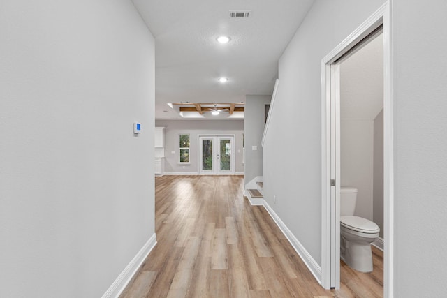 corridor with french doors, light wood-type flooring, visible vents, and baseboards