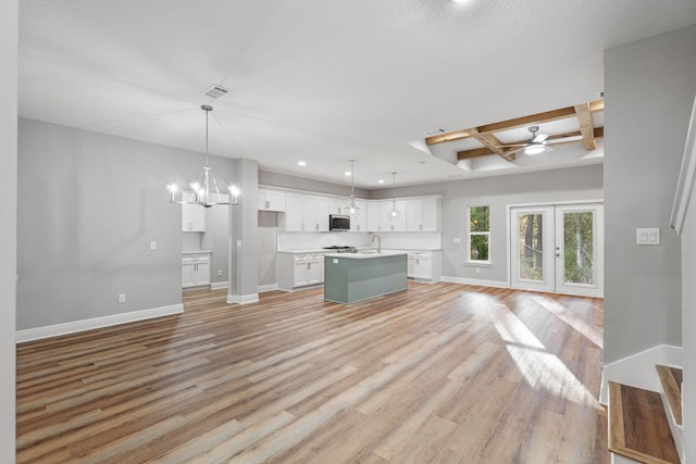 kitchen with white cabinets, open floor plan, hanging light fixtures, a kitchen island with sink, and light countertops