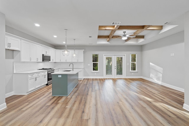 kitchen with stainless steel appliances, white cabinets, light countertops, a center island with sink, and pendant lighting