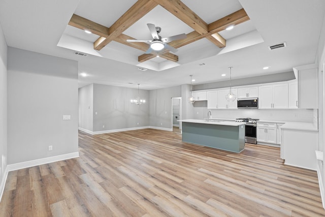 kitchen with a center island with sink, light countertops, open floor plan, white cabinetry, and gas range