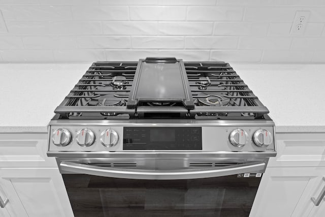 details featuring stainless steel gas stove, white cabinetry, light countertops, and backsplash