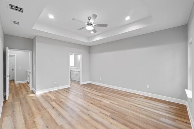 unfurnished bedroom featuring a tray ceiling, visible vents, light wood-style flooring, and baseboards