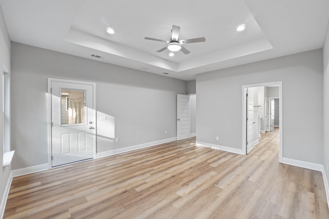 unfurnished room featuring a raised ceiling, light wood-style flooring, and baseboards