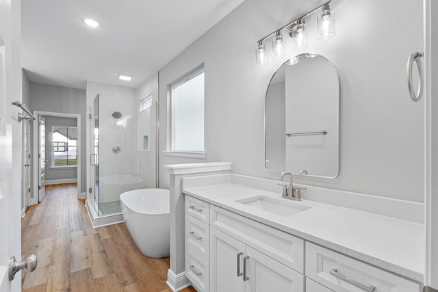 full bath with wood finished floors, vanity, baseboards, a freestanding bath, and a stall shower